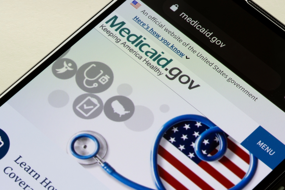 A black phone shows the webpage for Medicaid.gov where the tagline says Keeping America Healthy with an American flag heart outlined by a blue stethoscope.