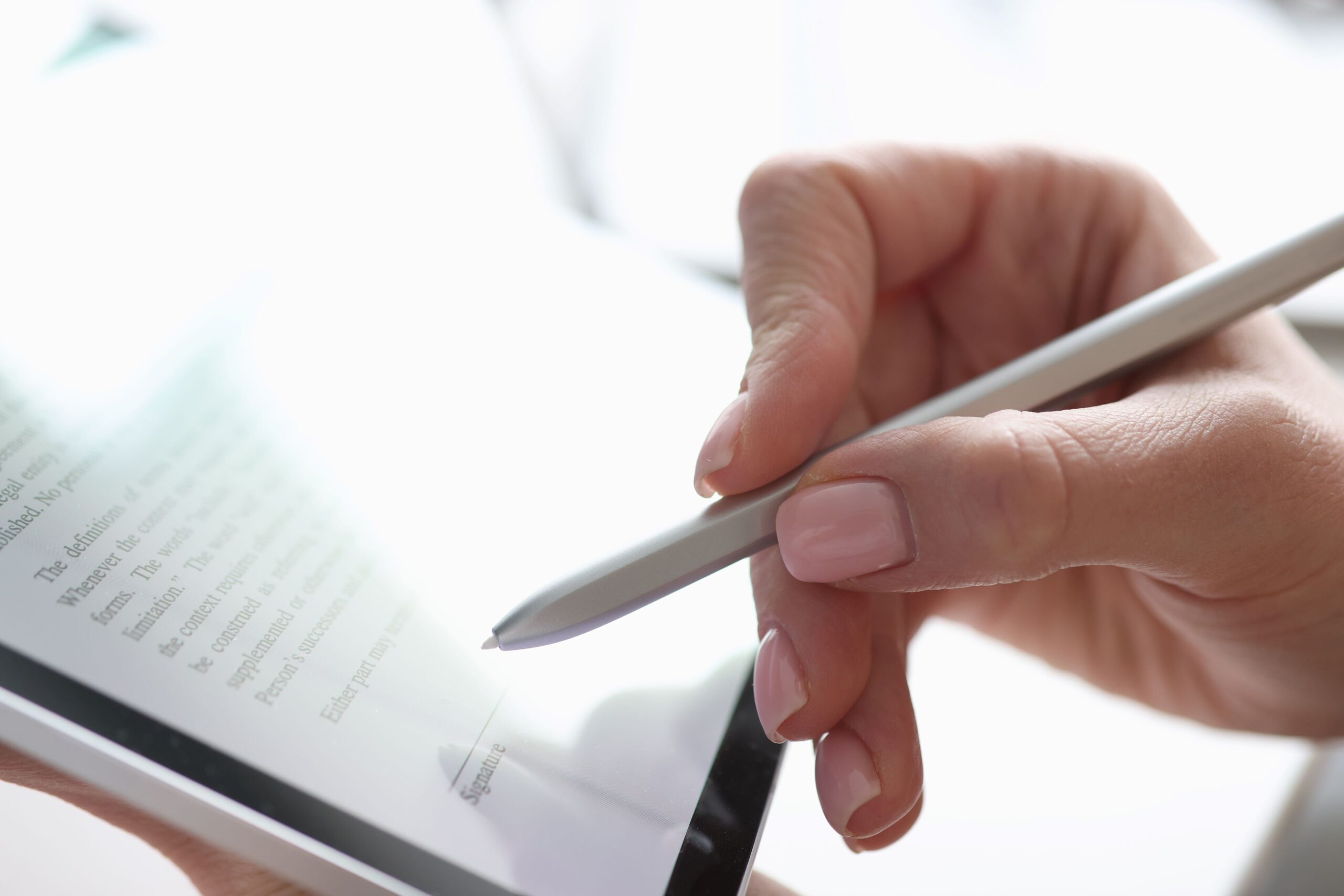 A ladies hand holds a silver pen in front off an iPad.